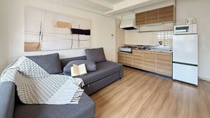A modern apartment with a grey sofa, a kitchen with wooden cabinets, and a white refrigerator. - Stylish 2-Story Apartment Near Atomic Bomb Dome (Hiroshima)