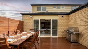 A patio with a wooden table set for dining, a barbecue grill, and a sliding glass door leading to a covered outdoor area. - Daintree Family Getaway- Beach, Aircon, Great yard (Ocean Grove)
