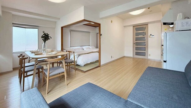 A compact hotel room with a bed, a dining table with chairs, a small kitchenette, and a large window. - Quiet 3BR Near Downtown Kitchen & Dining Equipped (Hiroshima)