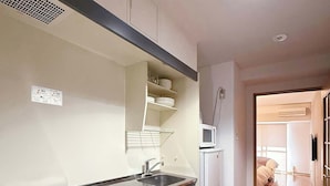 Een moderne keuken met een spoelbak, een magnetron en een koelkast. Er ligt een houten vloer en er is een deur naar een andere kamer.