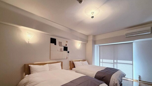 Een hotelkamer met twee bedden, een plafondventilator, een airconditioning en een groot raam met zonwering.