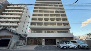 A multi-story hotel with a central entrance, parking area, and several cars parked in front.