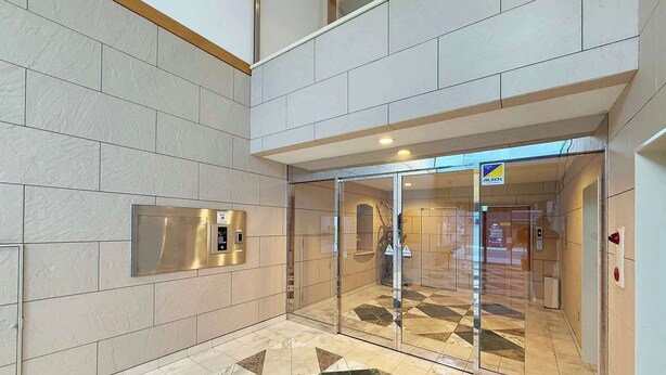 A modern lobby with a geometric patterned floor, a glass entrance, and a wall-mounted elevator control panel.