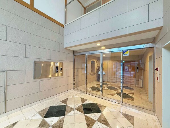 Un hall d’entrée moderne avec un sol à motifs géométriques, une entrée en verre et un panneau de commande d’ascenseur fixé au mur.