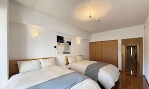 A hotel room with two beds, a wardrobe, a mirror, and a door leading to a hallway.