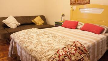 A bedroom with a bed, a sofa, and a nightstand with a lamp.