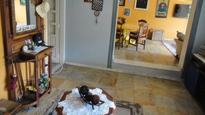 Une pièce comprenant un bureau en bois, une chaise, un miroir et une porte donnant sur une autre pièce où se trouvent une table à manger et des chaises.