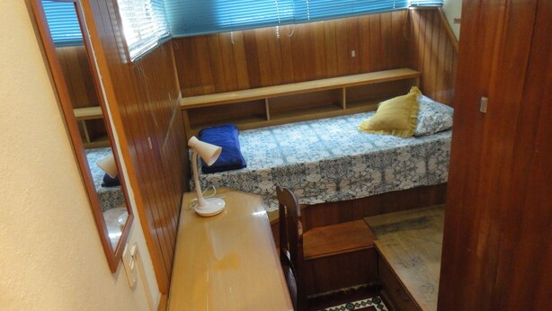 Ein kleines Zimmer mit einem Etagenbett, einem Schreibtisch mit Lampe und einem gemusterten Teppich.