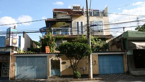 Un bâtiment à deux étages, doté d’un toit recouvert de tuiles, d’un réservoir d’eau sur le toit et d’une porte de garage bleue.