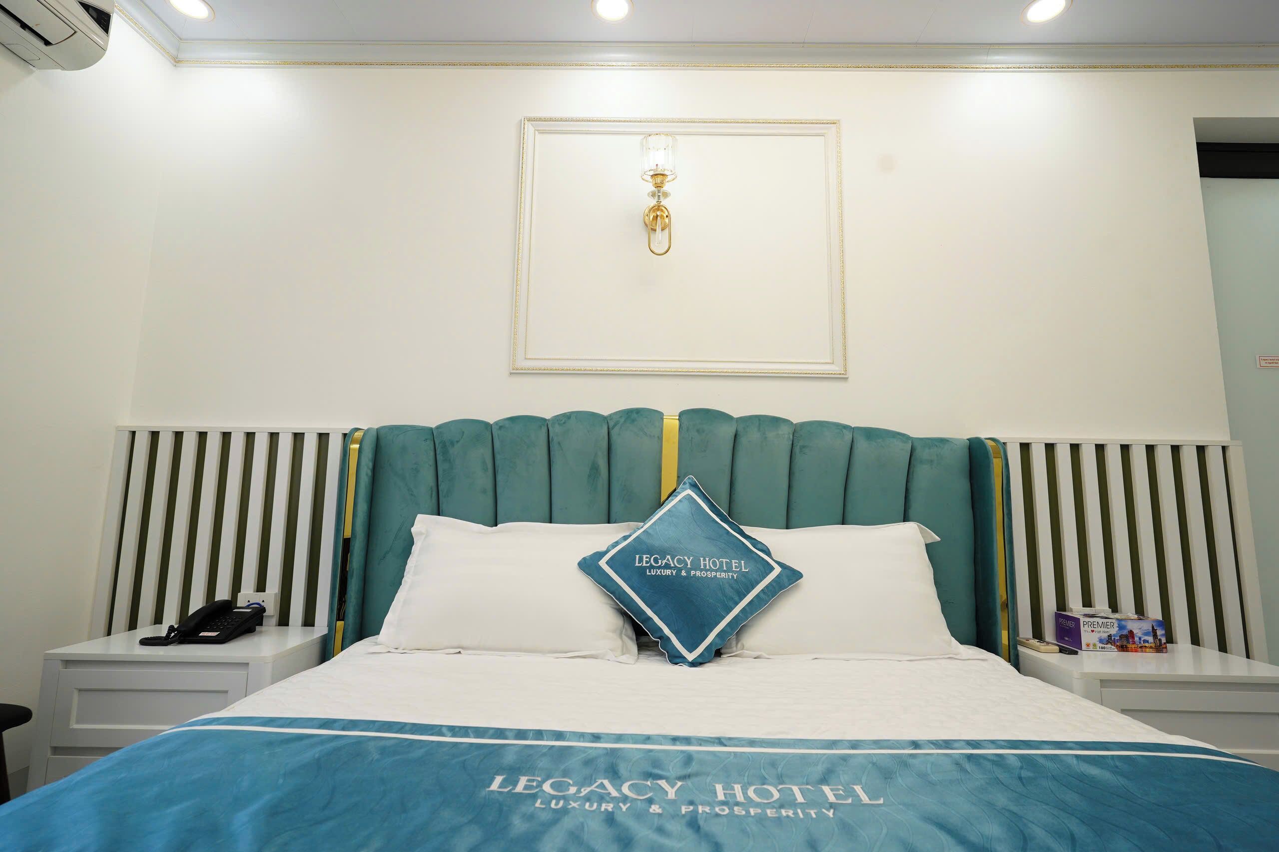 Une chambre d’hôtel avec un lit, une table de chevet, un téléphone, un tableau encadré et un panneau sur le mur.