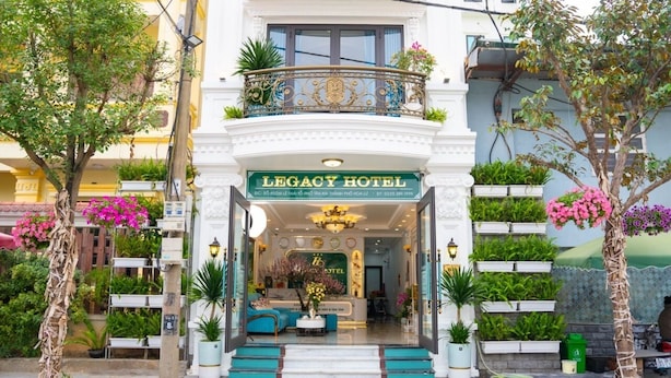 The exterior of the Legacy Hotel with a grand entrance, a balcony with decorative railings, and lush greenery around the building. - Legacy Hotel Ninh Binh (Hoa Lu)