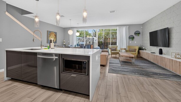 A modern kitchen with a central island, stainless steel appliances, pendant lighting, and a view to the outdoors. - No carpet 4BD Home: with Pool and Grill Near Magic (Kissimmee)