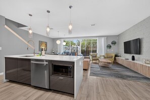 Cocina moderna con una isla central, electrodomésticos de acero inoxidable, iluminación colgante y vistas al exterior.