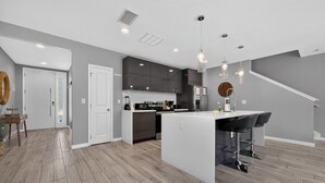 A modern kitchen with a central island, dark cabinetry, and pendant lighting. - No carpet 4BD Home: with Pool and Grill Near Magic (Kissimmee)
