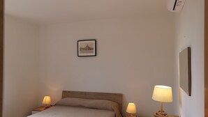 Une chambre à coucher avec un lit, deux tables de chevet avec des lampes, un tableau encadré au mur et une petite table de chevet avec une lampe.