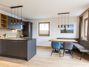 Una cocina moderna con armarios oscuros, una isla de madera y un comedor con un banco y dos sillas.