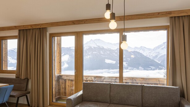 A cozy room with a sofa, a chair, a small table, and large windows offering a mountain view.