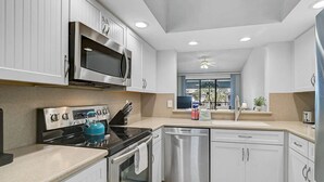 Cocina moderna con armarios blancos, electrodomésticos de acero inoxidable, un hervidor azul y una ventana con vistas.