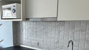 Une cuisine avec des armoires blanches, un plan de travail noir, un évier en acier inoxydable et un four à micro-ondes placé au-dessus du plan de travail.