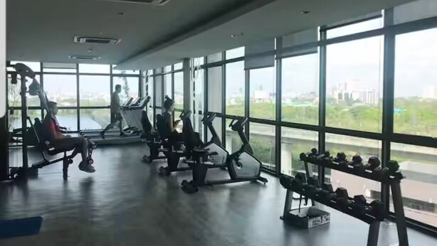 Une salle de sport équipée de divers appareils d’exercice, dotée de grandes fenêtres et offrant une vue sur la ville.
