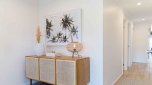 A hallway with a wooden console table, a framed picture of palm trees, and a woven lamp. - Rose by Omaru Farm (Cowes)