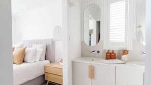 A bedroom with a bed, bedside table, and a nightstand. The room has a window with blinds, a mirror, and a white wardrobe with a mirror above the door. - Rose by Omaru Farm (Cowes)