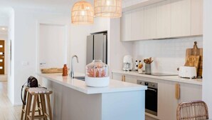A modern kitchen with white cabinetry, a central island, pendant lighting, and a built-in oven. - Rose by Omaru Farm (Cowes)