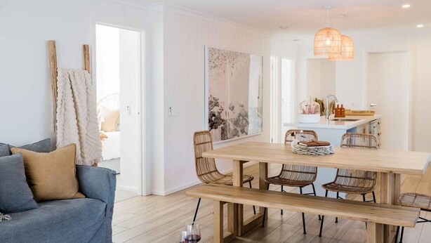 A modern living room with a sofa, a dining table with chairs, and a kitchen area with a hanging light fixture. - Rose by Omaru Farm (Cowes)