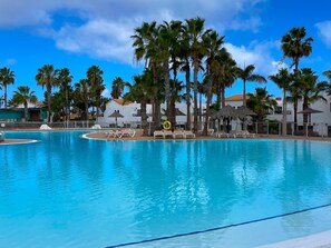 Una piscina amplia con sillones de descanso y palmeras.