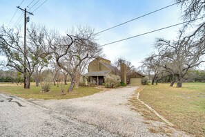 A house with a gravel driveway, surrounded by leafless trees and a clear sky.