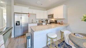 Una cocina moderna con armarios blancos, electrodomésticos de acero inoxidable y una isla central con taburetes.