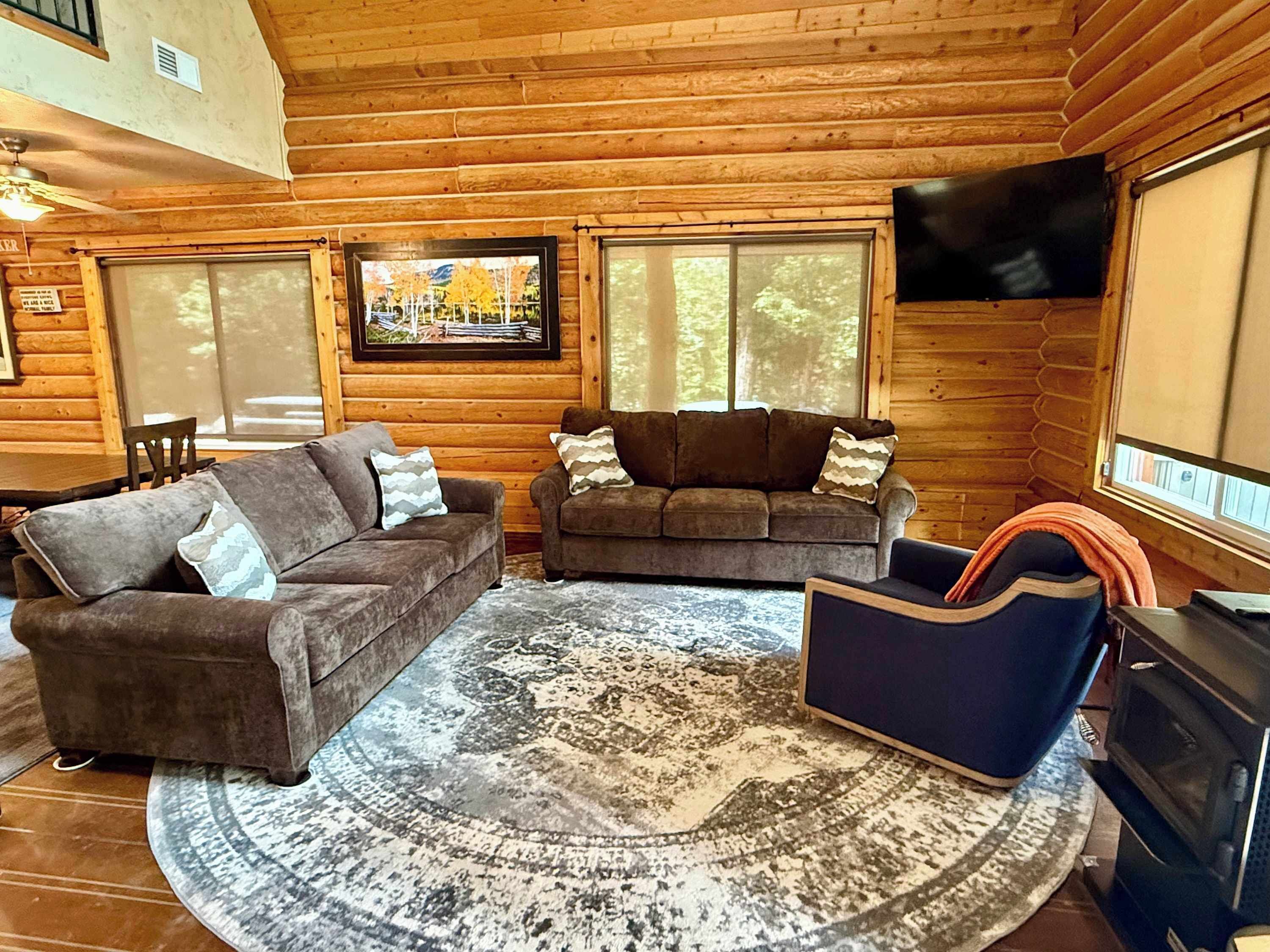 A log cabin interior with two sofas, a patterned rug, a television, and a fireplace.