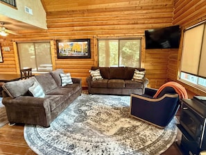 A log cabin interior with two sofas, a patterned rug, a television, and a fireplace.