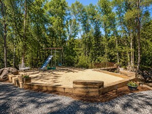 A playground with a slide and swings, surrounded by trees.