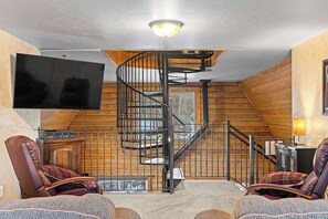 A cozy living room with a wooden staircase, leather chairs, a flat-screen TV, and a fireplace. - Evy's Cabin, 2 Miles to National Forest Land – Snowmobiling and Side-by-Siding (Heber City)