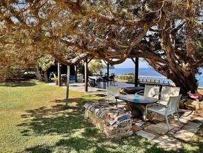 Area patio esterna con tavoli e sedie, una panchina in pietra e vista sul mare.