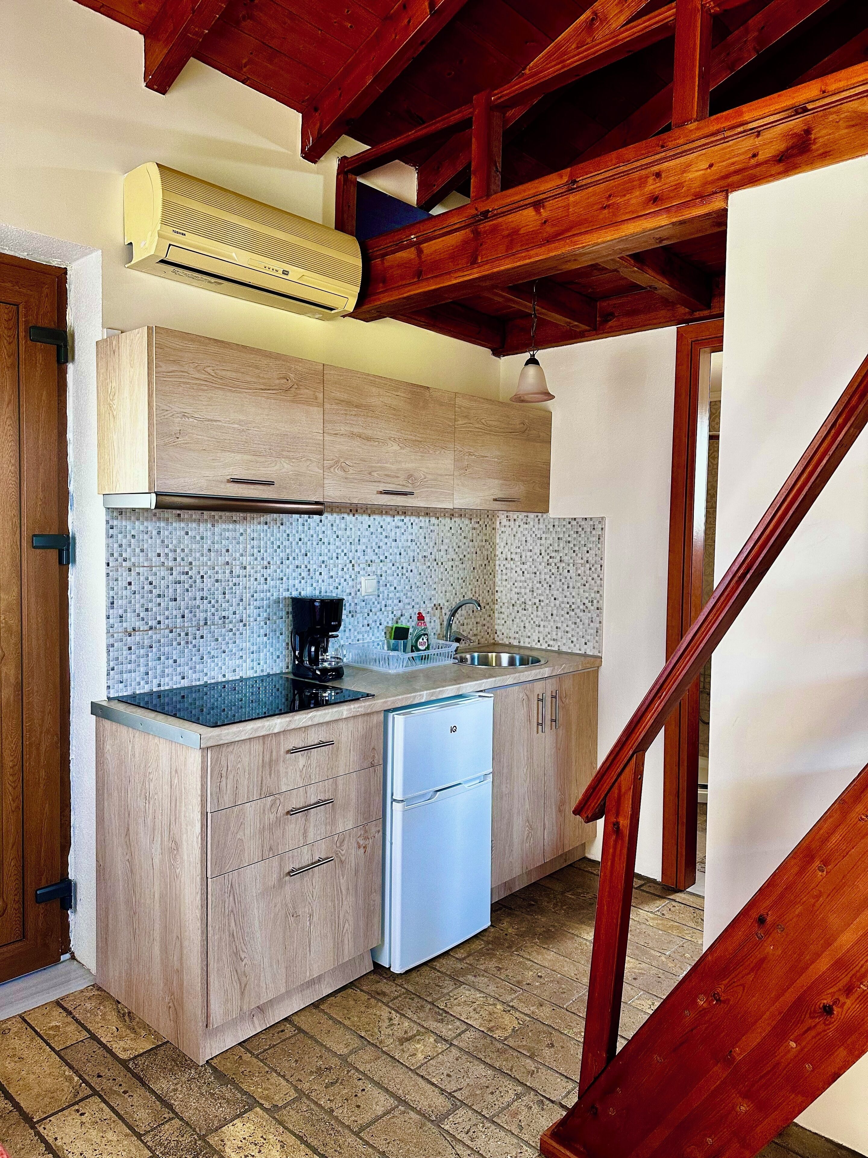 A compact kitchen with wooden cabinets, a built-in dishwasher, a tiled backsplash, and a wooden ceiling structure.