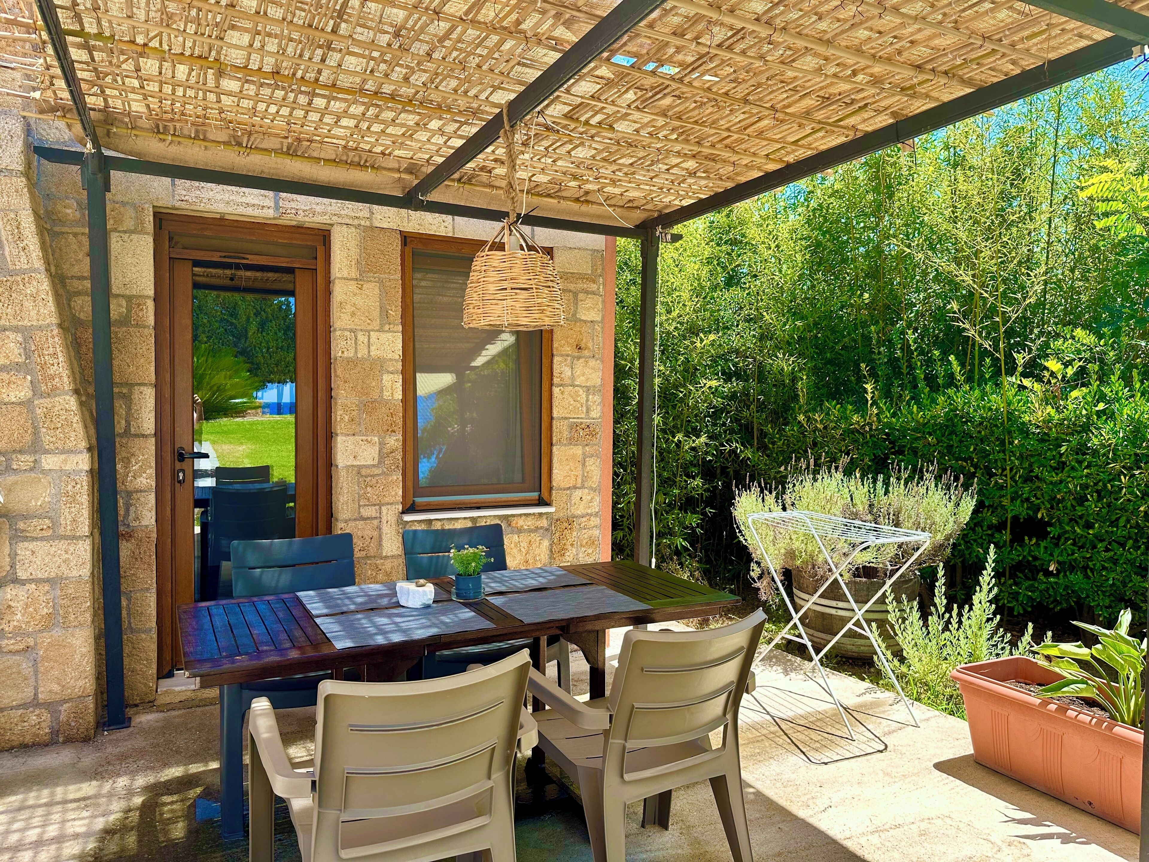 Een terras buiten met een tafel, stoelen, een hanglamp en uitzicht op een tuin.