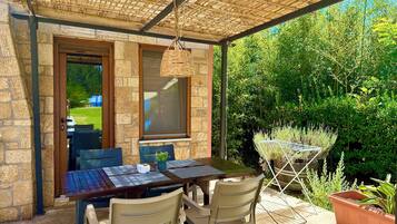 Een terras buiten met een tafel, stoelen, een hanglamp en uitzicht op een tuin.