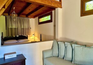 Una camera da letto con soffitto in legno, un letto con testiera, una finestra con tende, un comodino con scatola di fazzoletti e un divano dai toni chiari.