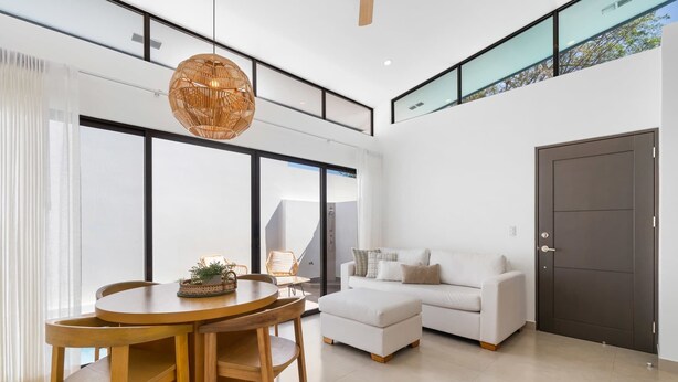 Una sala de estar moderna con una mesa redonda de madera, un sofá blanco y un amplio ventanal.