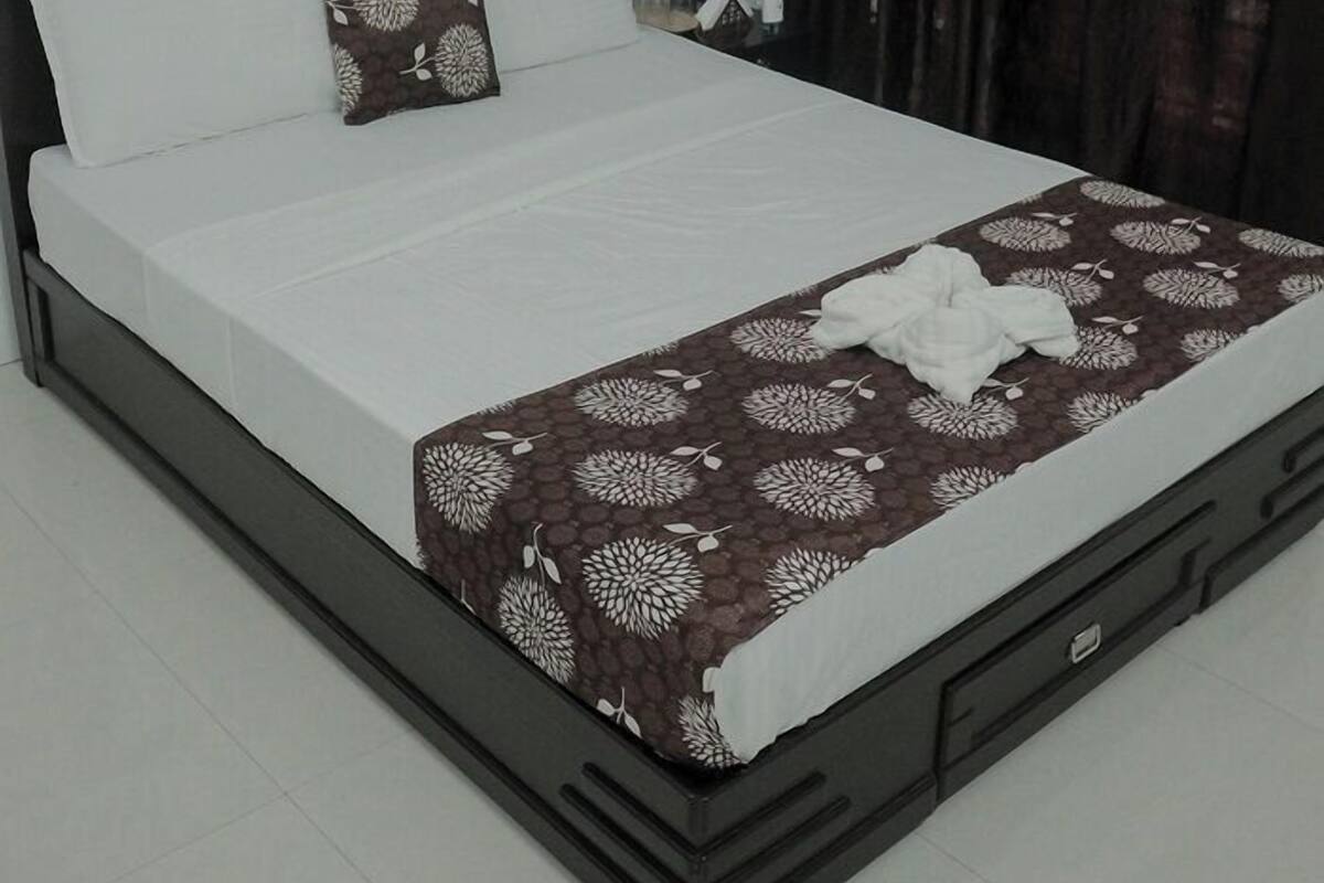 Una cama bien tendida con una colcha estampada, un cabecero de madera y una mesita de noche con agua embotellada.