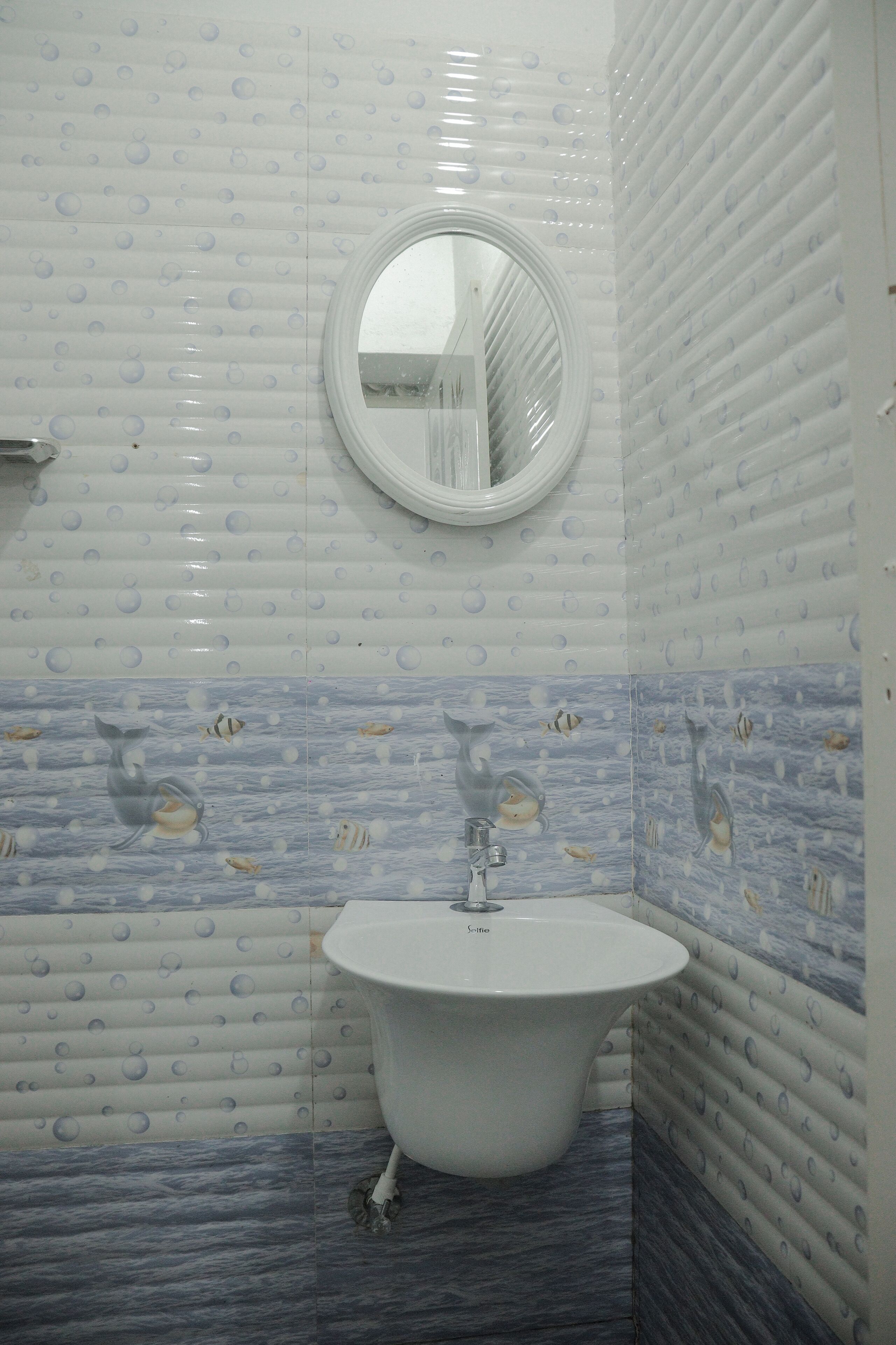 Een badkamer met een ronde spiegel, een wit wastafelmeubel en blauw-witte betegelde vloer.