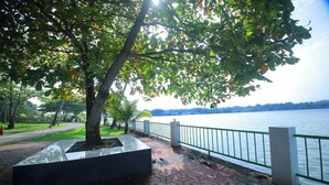 A paved walkway with a railing overlooking a body of water, surrounded by trees and a grassy area.