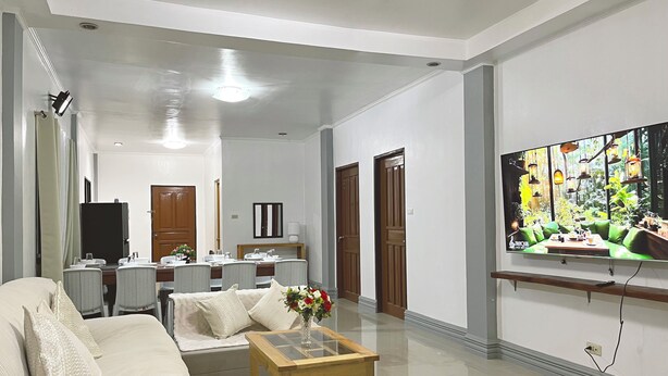 A spacious living area with a sofa, a coffee table, and a dining table set for four. There is a large window with a view of greenery. - Ivory Bloom - Spacious 4-BR w/ WiFi, AC, Large Space in Puerto Princesa, Palawan (Puerto Princesa)