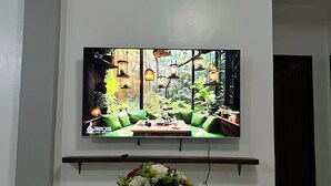 A television mounted on a wall with a wooden shelf below it. - Ivory Bloom - Spacious 4-BR w/ WiFi, AC, Large Space in Puerto Princesa, Palawan (Puerto Princesa)