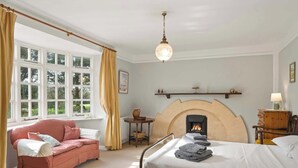 A bedroom with a bed, a pink sofa, a fireplace, and a window with curtains. - Homely Cottage & Garden nr Praa Sands & Marazion (Rosudgeon)