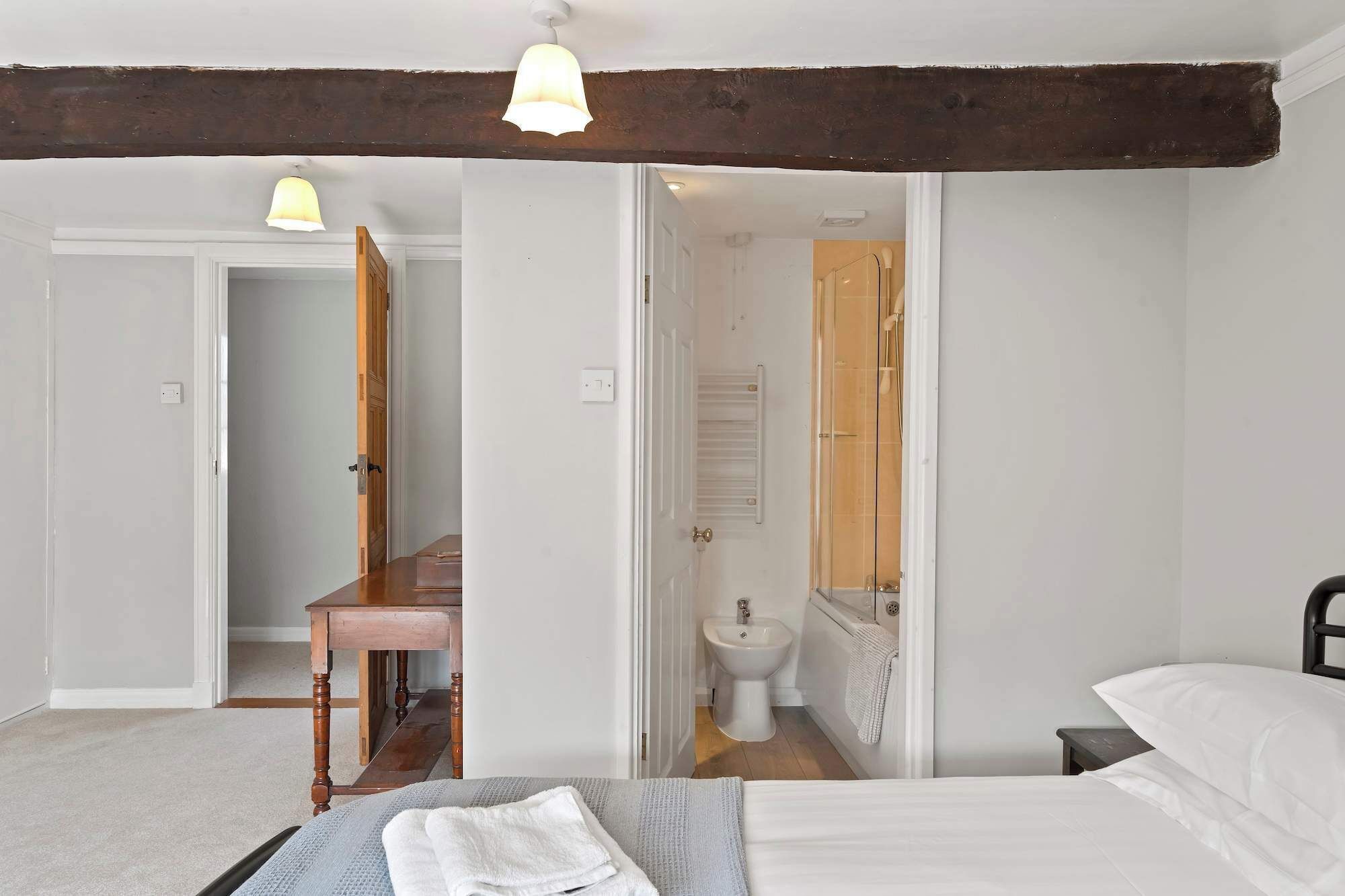Een slaapkamer met een bed, een nachtkastje, een houten stoel, en een badkamer met toilet, een bidet en een bad.