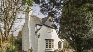 A quaint white cottage with a steeply pitched roof, a visible chimney, and a small garden with potted plants and a stone pathway leading to the entrance. - Homely Cottage & Garden nr Praa Sands & Marazion (Rosudgeon)