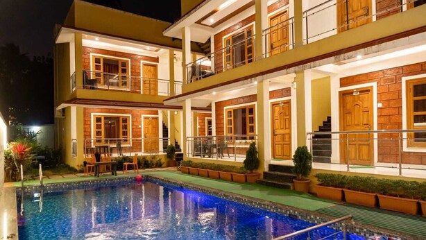 Un hotel de varios pisos con piscina, mobiliario exterior y una entrada bien iluminada.